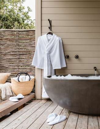 close up of a bath tub with a white rob hanging on the wall, white slippers and a beach bag on the floow at the spa at Carmel Valley Ranch